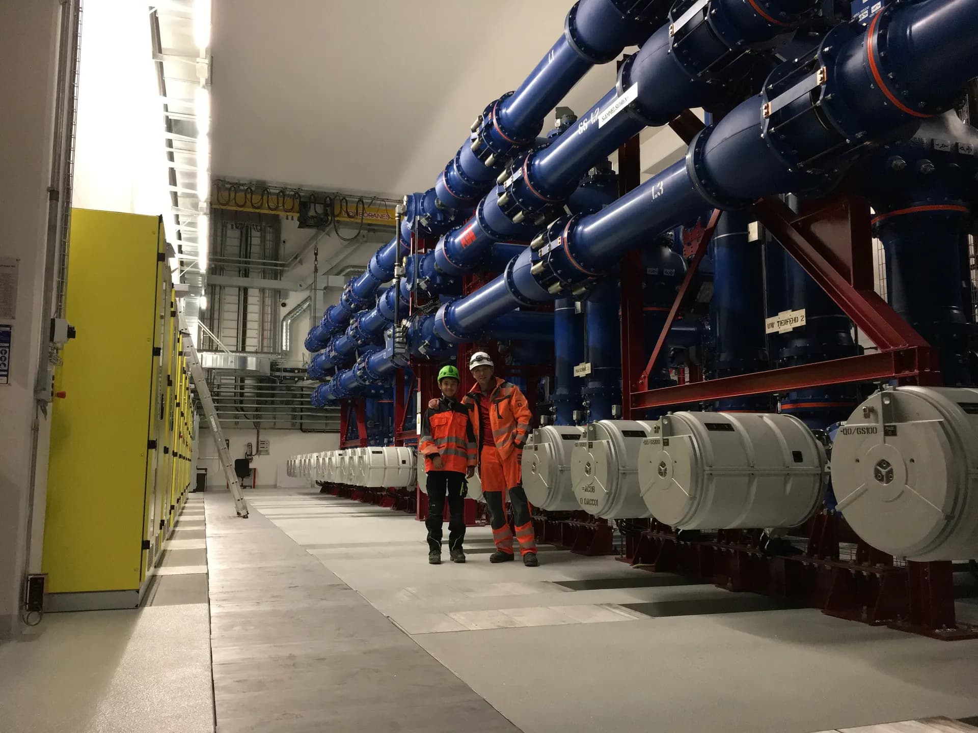 Zwei Monteure vor den blauen Generatorableitungen in der Kavernenzentrale des Pumpspeicherwerks Limmern